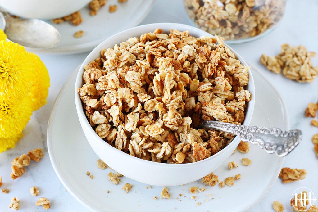 Bowl of French Toast granola with a spoon and yellow flowers next to it. 