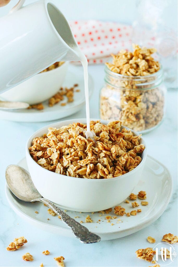 Gorgeous photo of a bowl of French toast granola and small pitcher of almond milk being poured over it. 