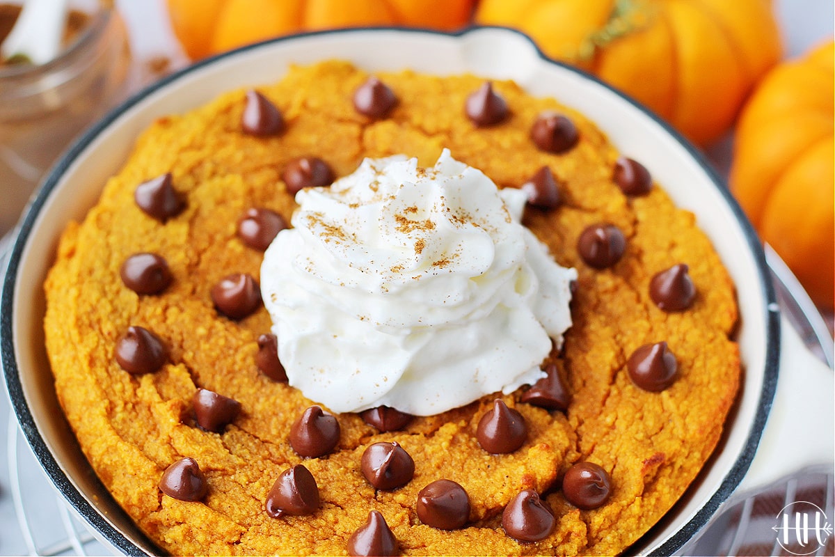 Whipped cream and cinnamon on top of a pumpkin cake in a cast iron pan.