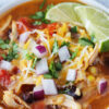 Up close photo of a bowl of chicken enchilada soup topped with lime wedges.