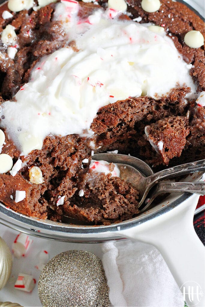 Up close shot of two spoons in the ooey gooey cake topped with whipped cream.