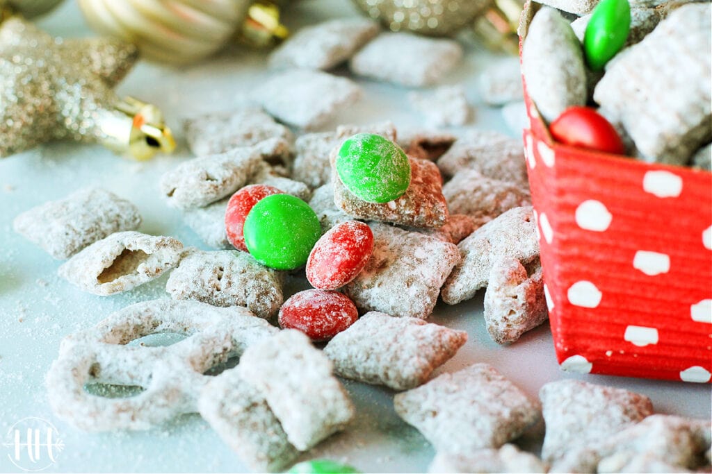 Holiday Muddy Buddy Mix with red and green candy coated chocolates scattered on a white surface.
