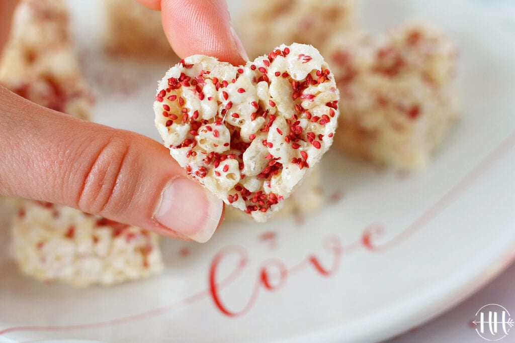 Heart shaped rice krispies treat held over a valentines day plate. 
