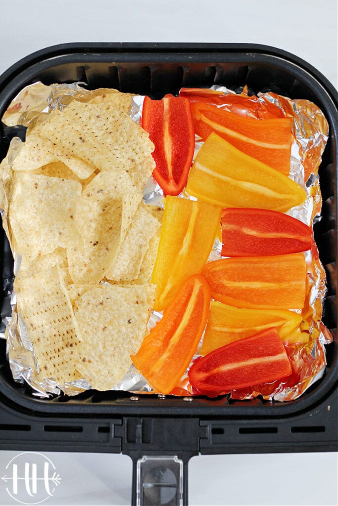 Cosori air fryer lined with aluminum foil topped with tortilla chips and halved mini bell peppers. 