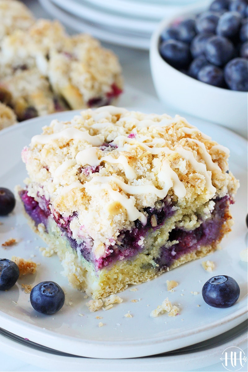 A slice of blueberry coffee cake with crumble topping on a white plate.