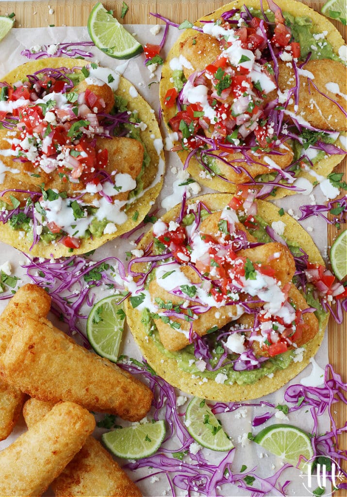 Bird's eye view of 3 Air Fryer Fish Tostadas on a cutting board topped with colorful veggies.
