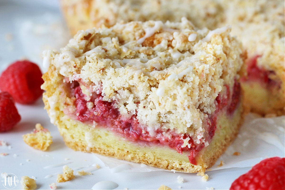 A slice of low sugar raspberry coffee cake with crumble topping and icing drizzle.