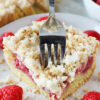 A fork slicing through a piece of layered coffee cake with raspberries.