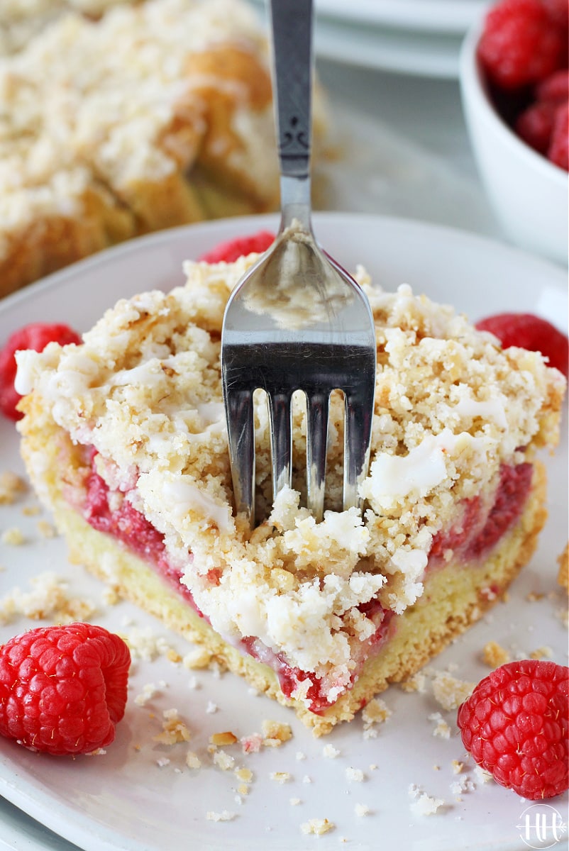 A fork slicing through a piece of layered coffee cake with raspberries.