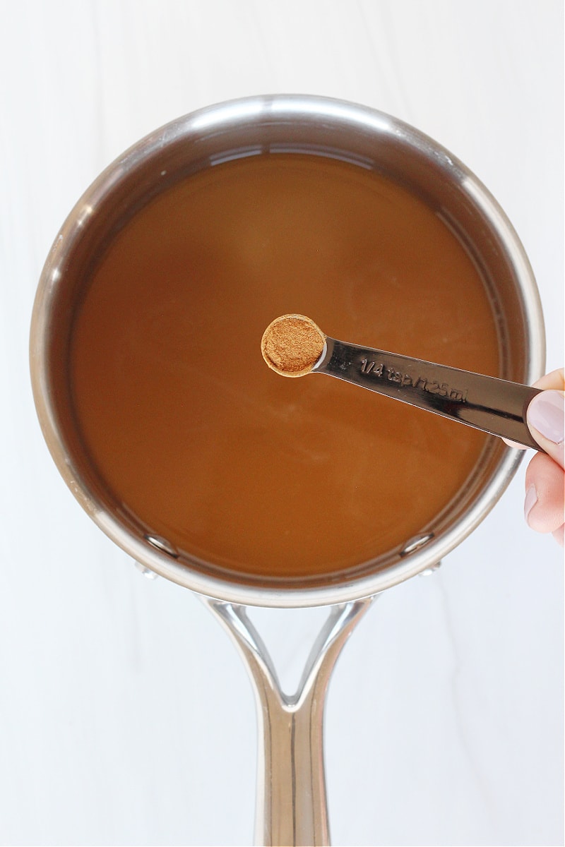A quarter teaspoon filled with cinnamon over a pan of bone broth hot cocoa.