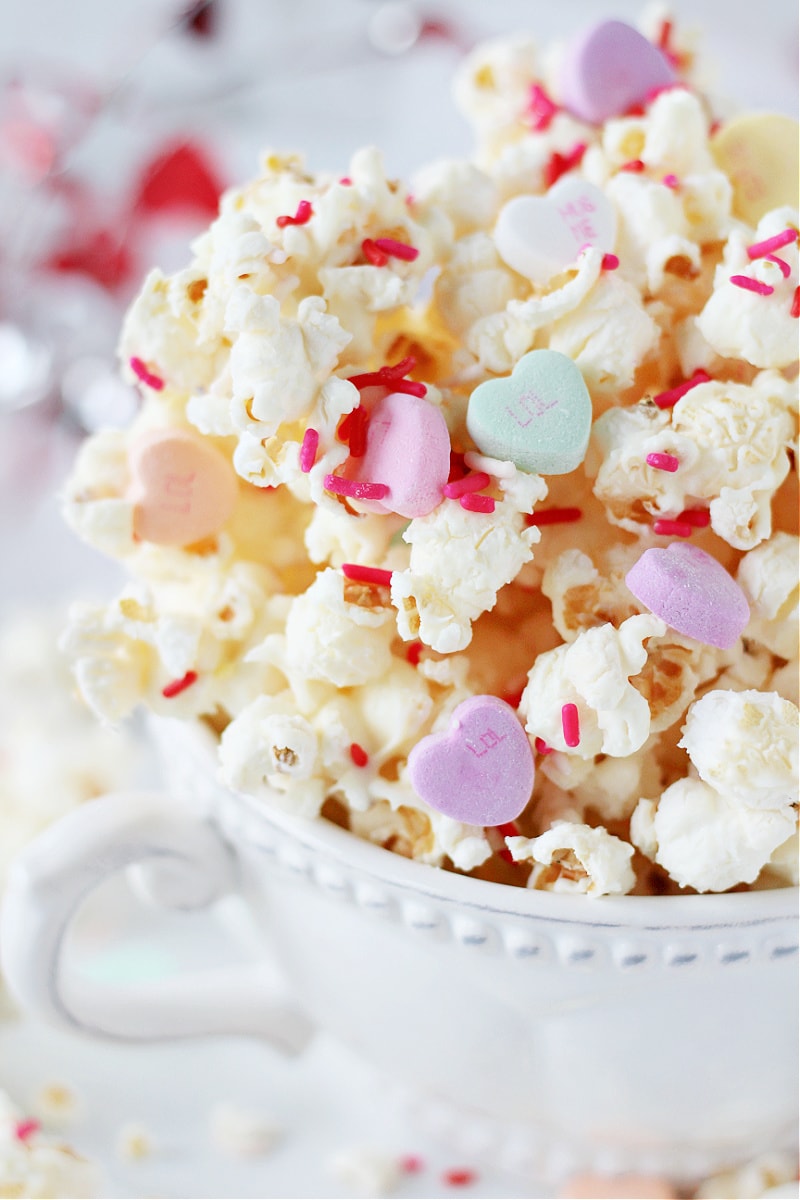 Side shot of Easy Valentine's Popcorn with white chocolate drizzle and sprinkles in white bowl.