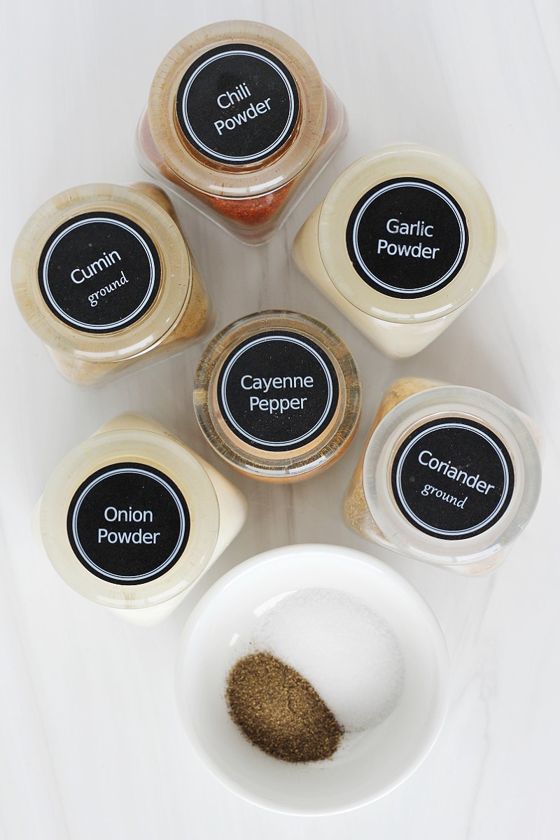Overhead photo of labeled spice jars with salt and pepper on a white countertop.