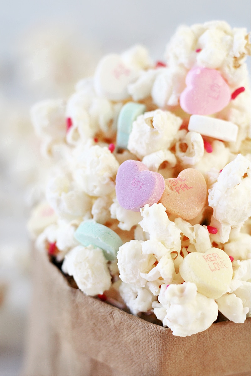 Up close photo of Easy Valentine's Popcorn with conversation hearts in a paper bag.