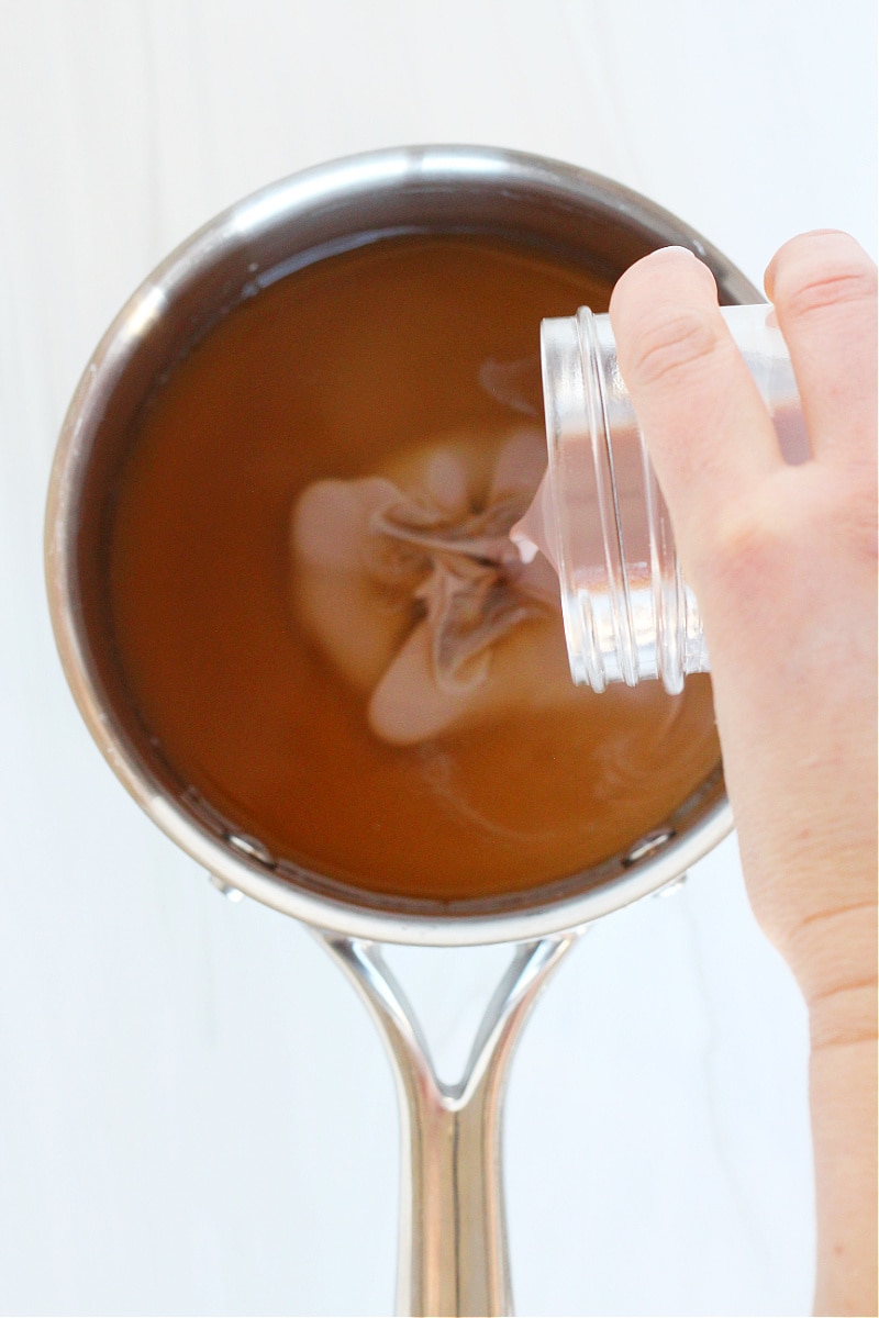 A woman's hand pouring low sugar chocolate milk into a soup pot of bone broth.