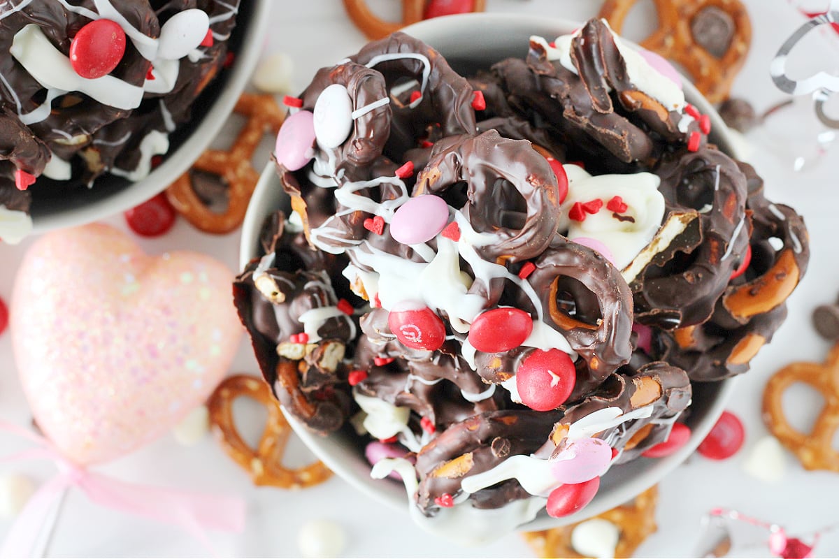Overhead photo of a bowl of dark chocolate covered pretzels, Valentine M&Ms, and heart sprinkles.