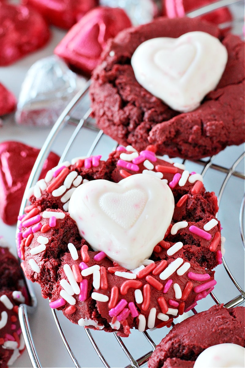 Valentine sprinkles covered red velvet cookie with a white chocolate heart on top.