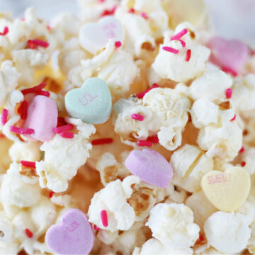 Up close photo of white chocolate Valentine's popcorn with pink sprinkles and conversation hearts.