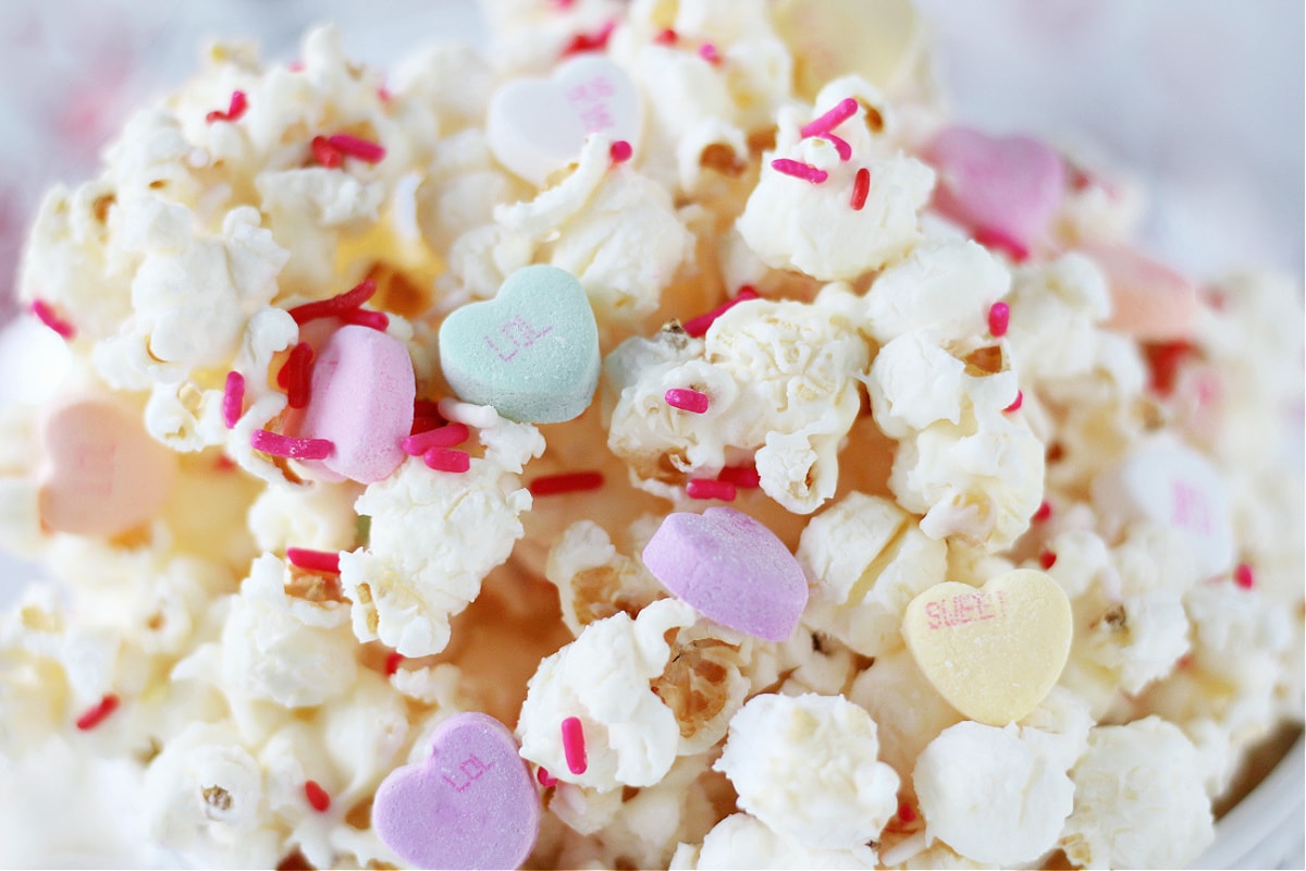 Up close photo of white chocolate Valentine's popcorn with pink sprinkles and conversation hearts.