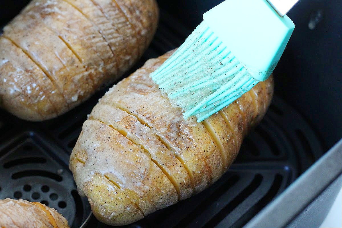 Brushing seasoned melted butter on a hasselback potato in the air fryer.