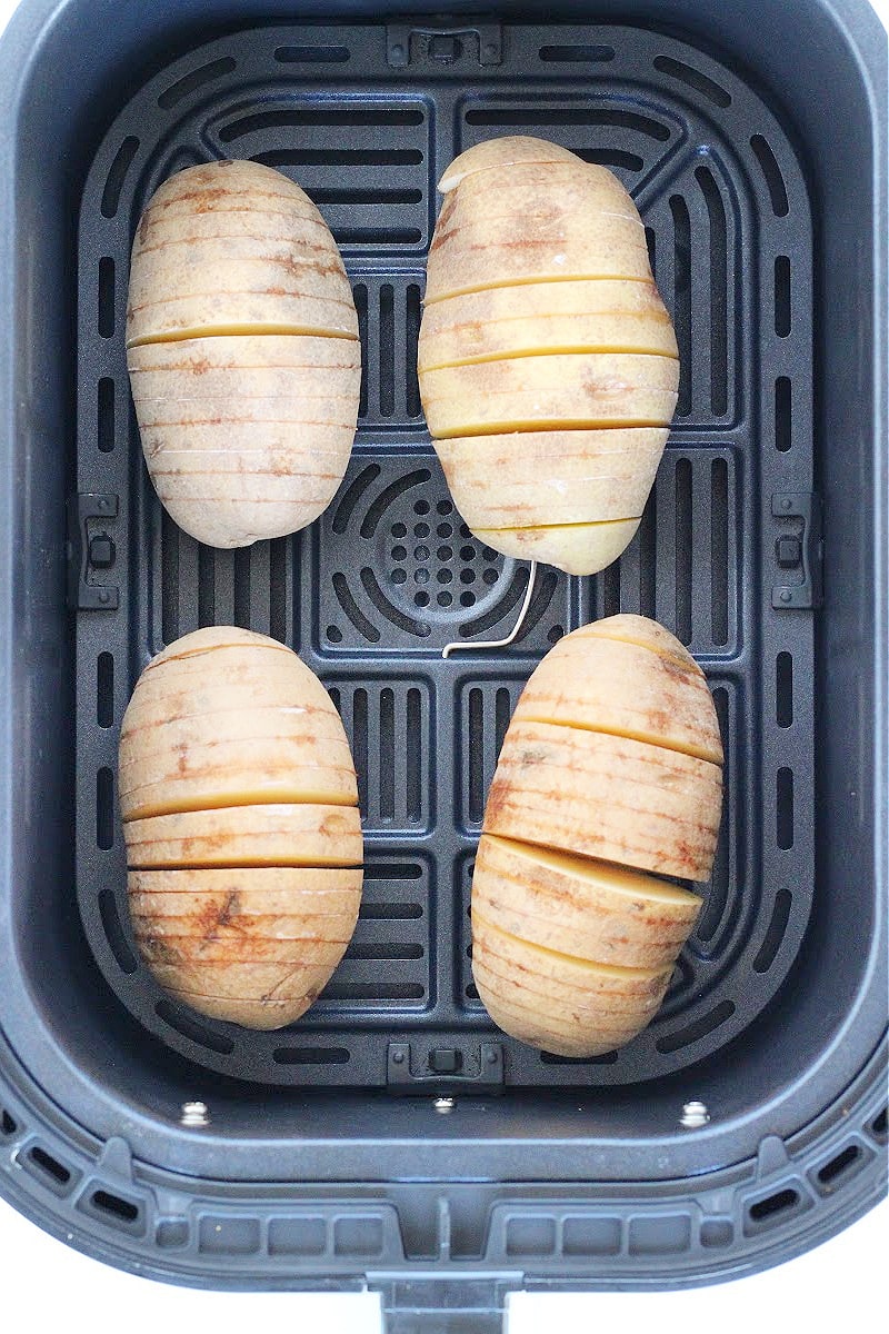 Overhead photo of four sliced hasselback potatoes in an air fryer basket.