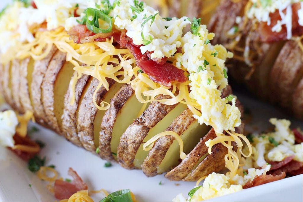 Up close photo of breakfast air fryer hasselback potatoes topped with grated eggs.