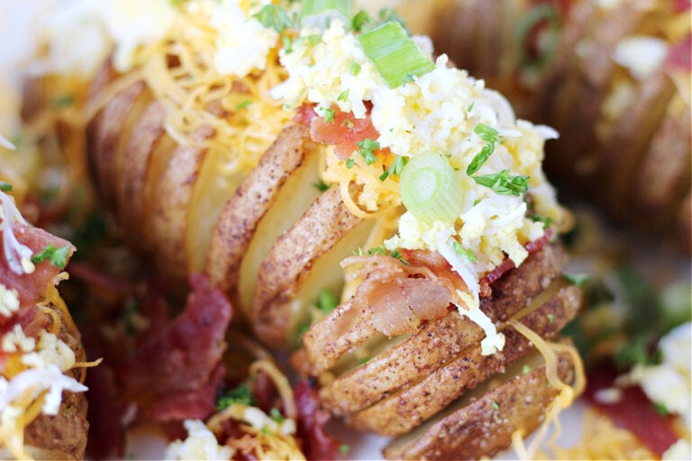 Green onion, shredded cheese, grated egg, and bacon topping a hasselback potato.