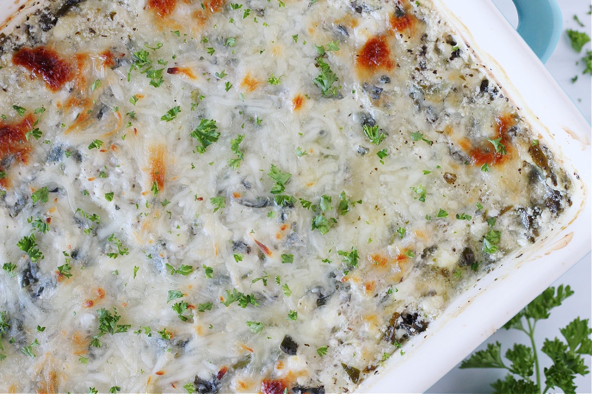 Overhead photo of a pan of hot spinach artichoke dip garnished with chopped parsley.