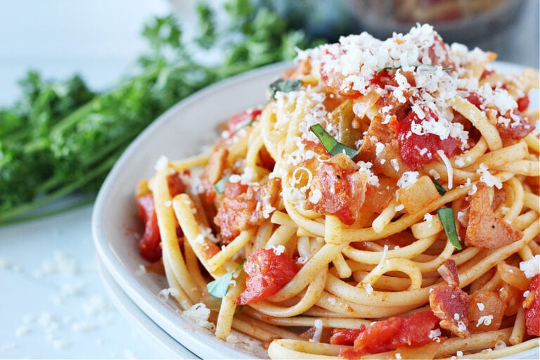 Up close photo of Pasta All'Amatriciana on a white plate topped with Parmesan cheese.