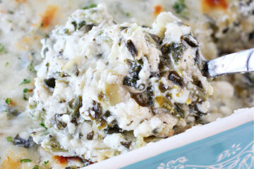 A spoon in a ceramic dish of baked creamy spinach and artichoke dip.