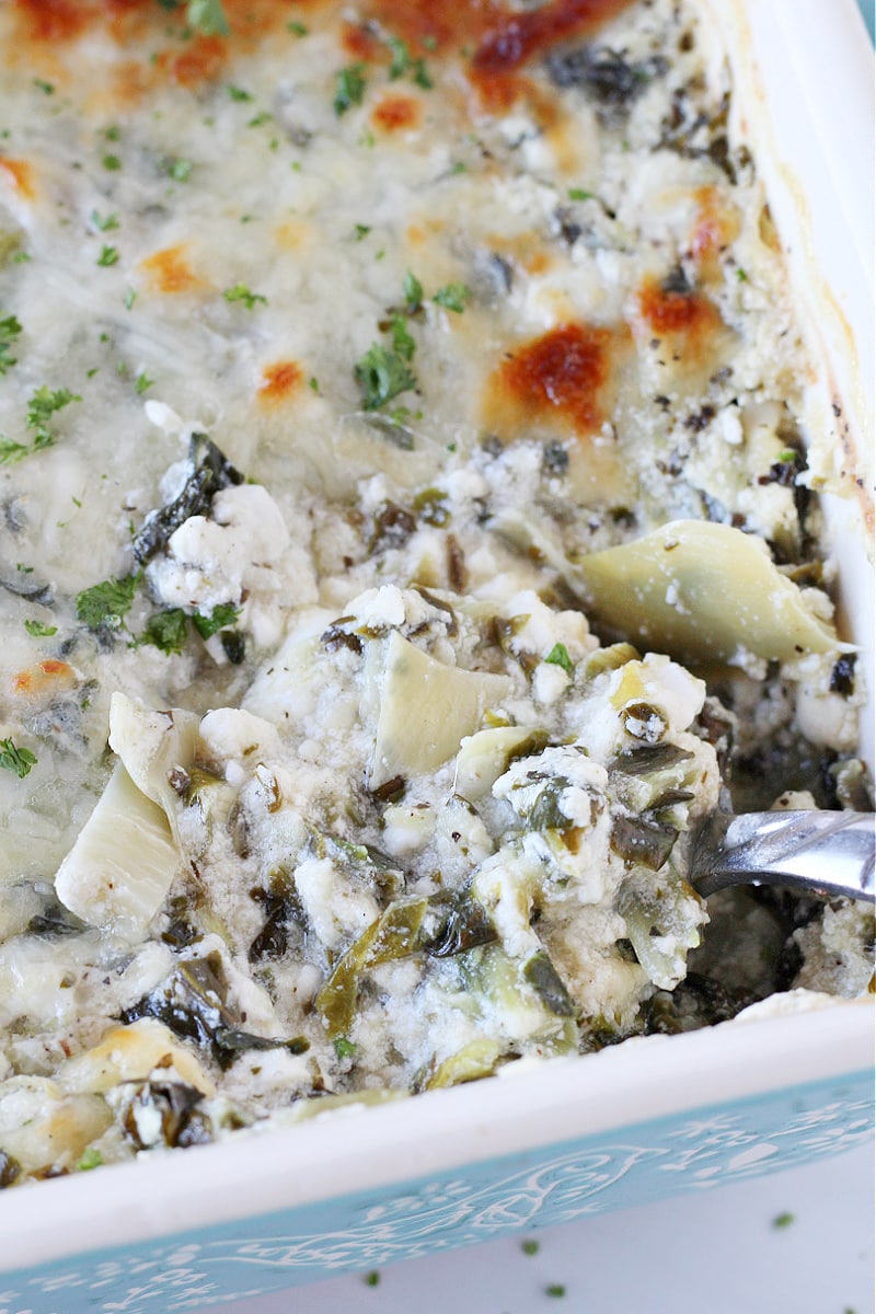 Hot spinach and artichoke dip in a ceramic pan with a spoon digging in.