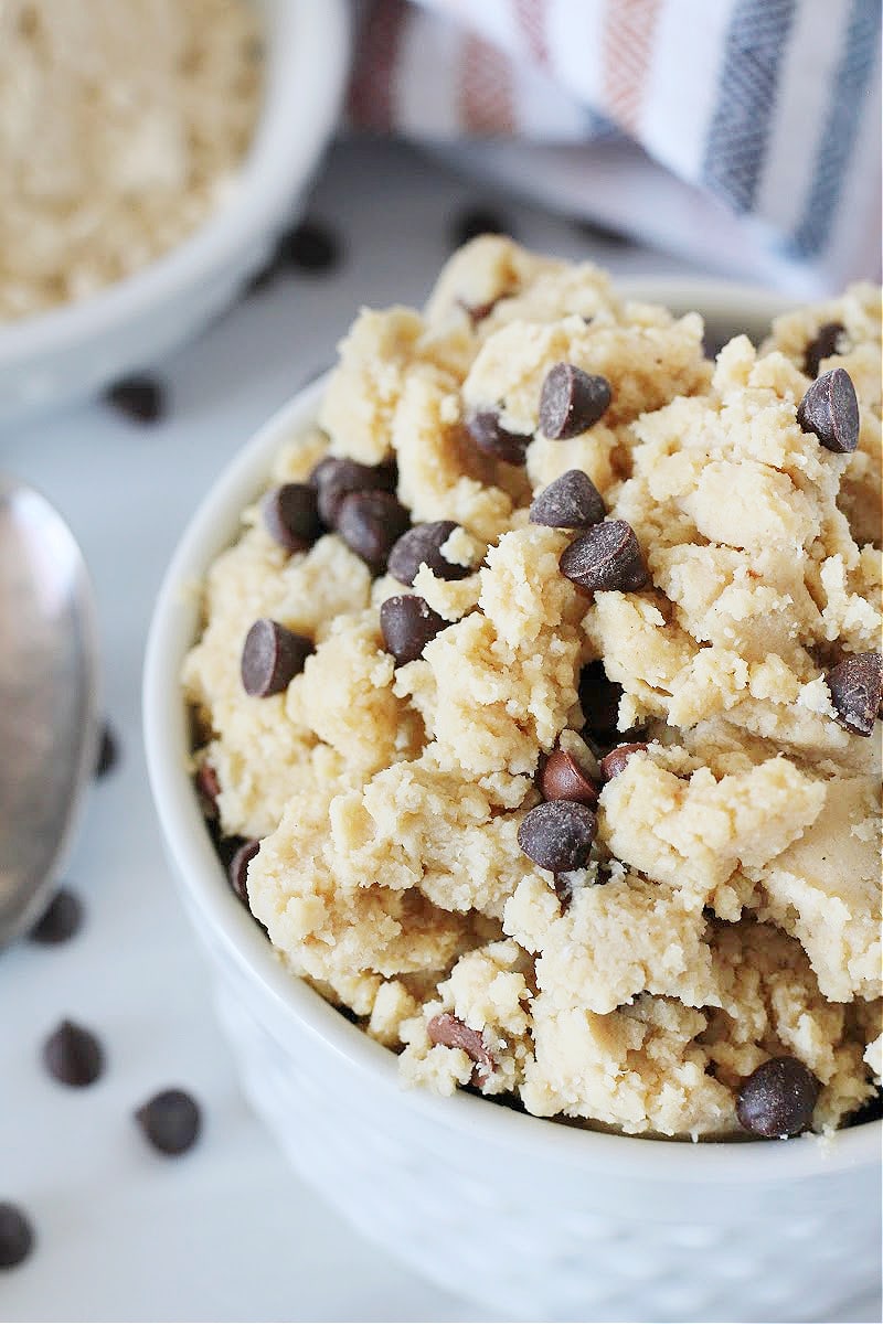 Up close side view of edible chocolate chip cookie dough in a white bowl.