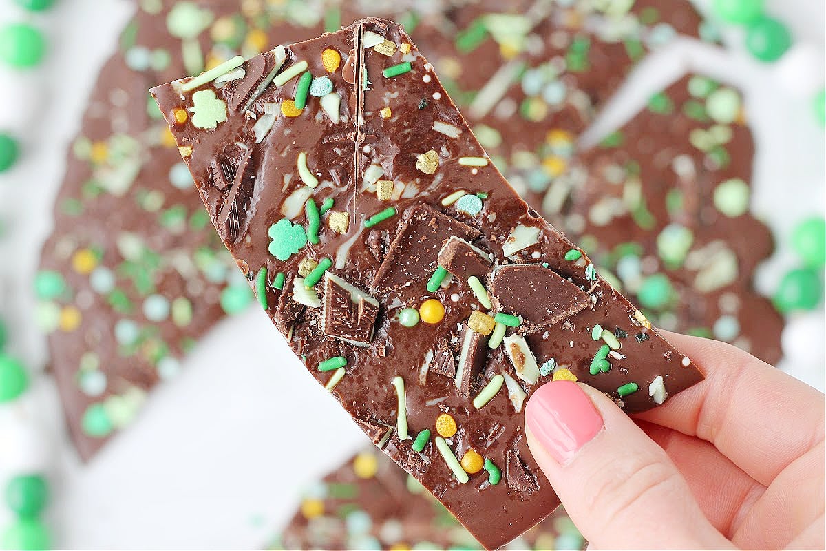 A woman's hand holding up a piece of chocolate St. Patrick's Day Leprechaun Bark.