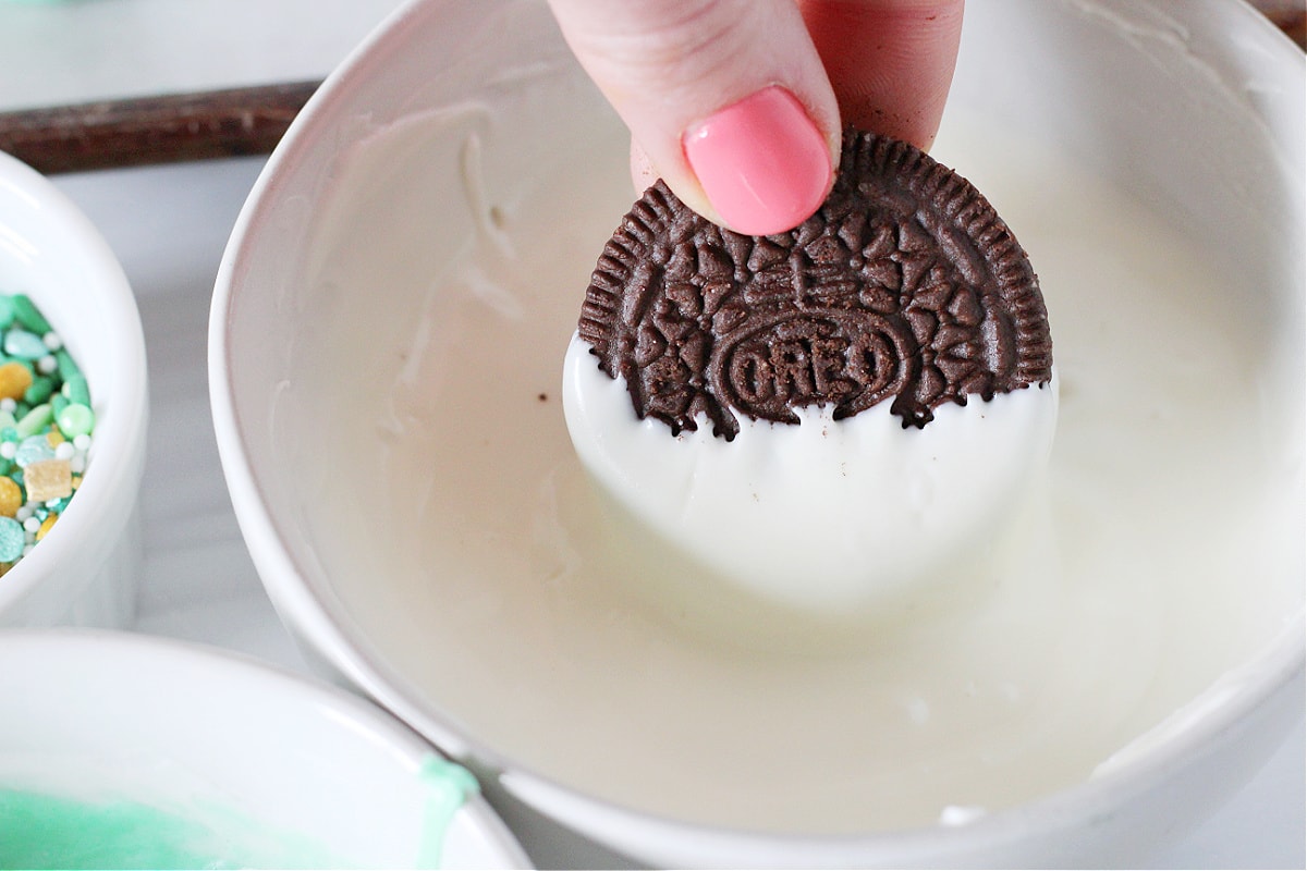 Half an Oreo being dipped in a bowl of melted white chocolate.