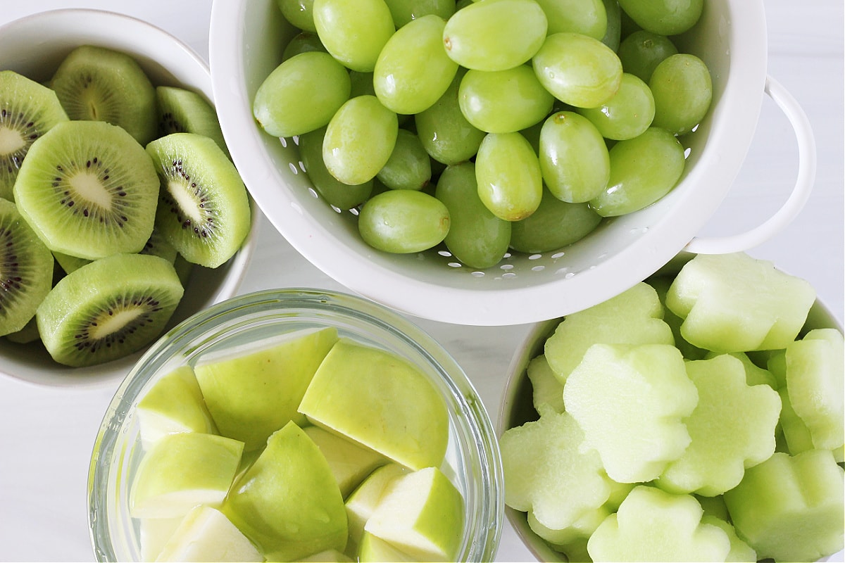 Overhead photo of green grapes, cut green apples, sliced kiwi and honeydew melon shamrocks.