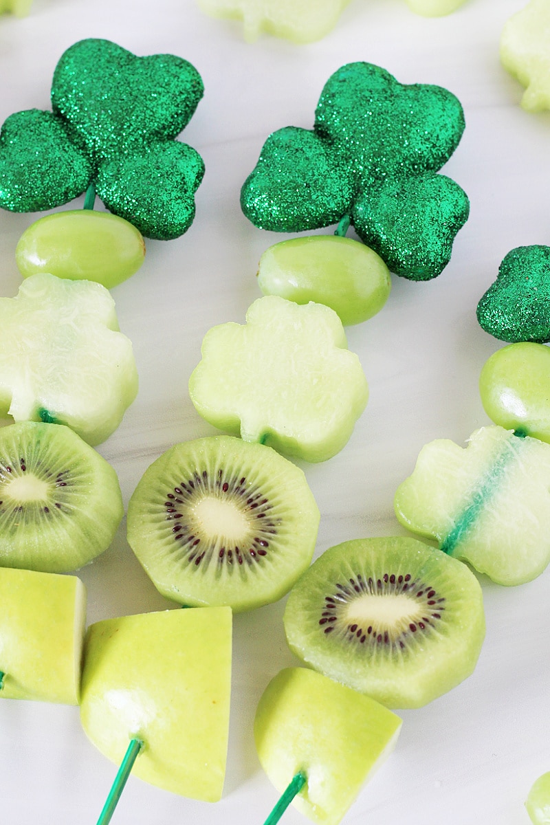Overhead photo of three St. Patrick's Day Fruit Kabobs on a white countertop.