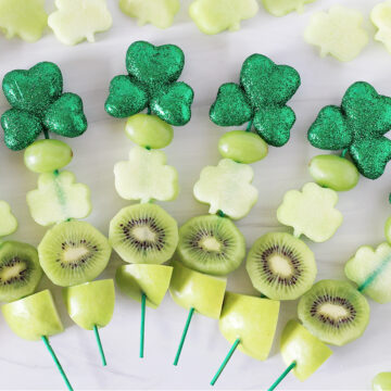 Overhead photo of six St. Patrick's Day Fruit Kabobs surrounded by honeydew melon shamrocks.