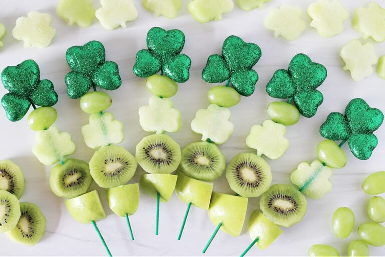 Overhead photo of six St. Patrick's Day Fruit Kabobs surrounded by honeydew melon shamrocks.