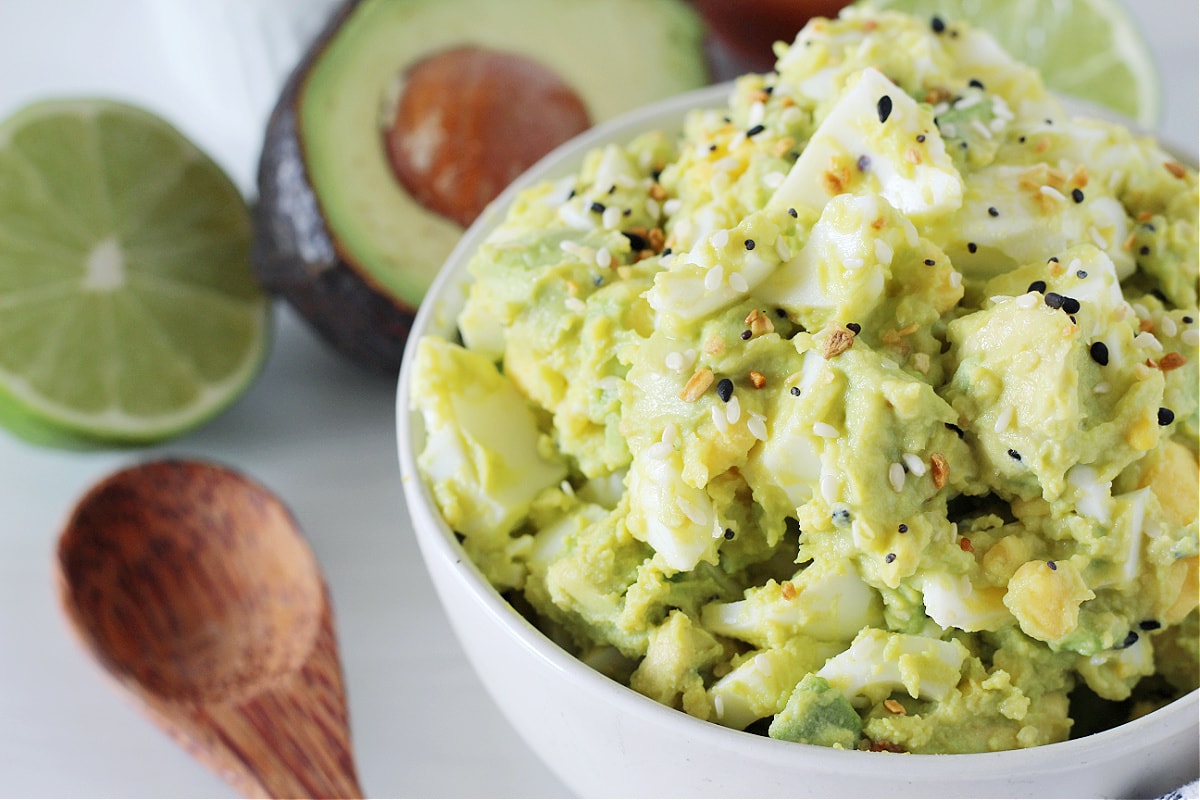 Side shot of low carb avocado egg salad in a white bowl garnished with EBTB.