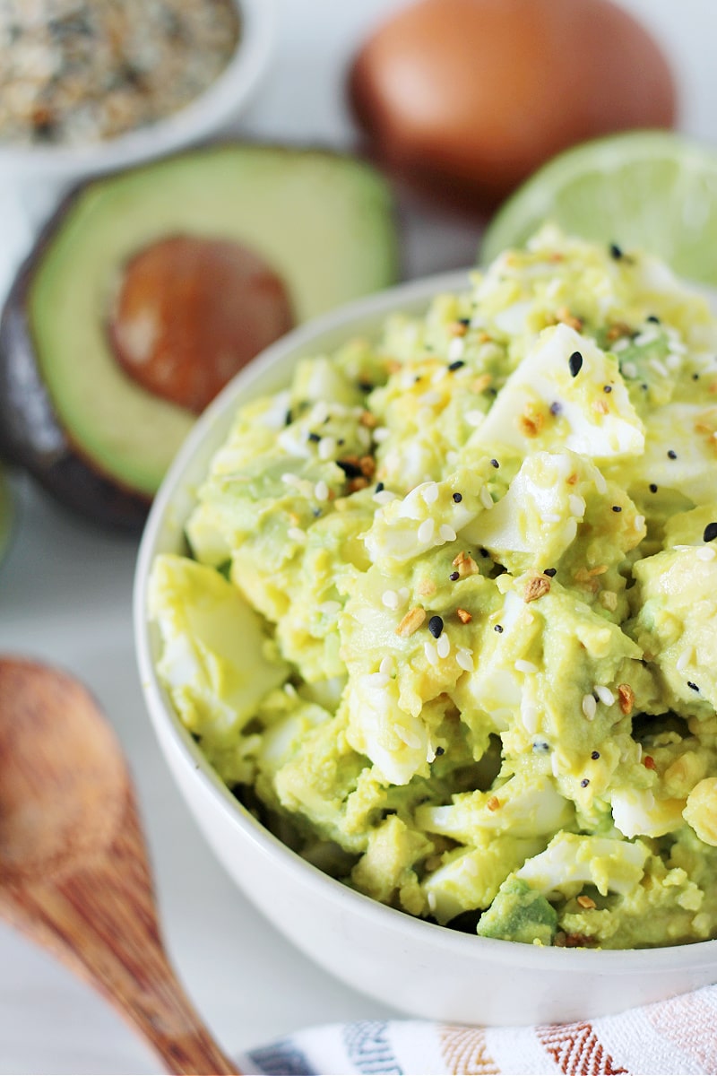 Side shot of easy avocado egg salad in a white bowl garnished with EBTB.
