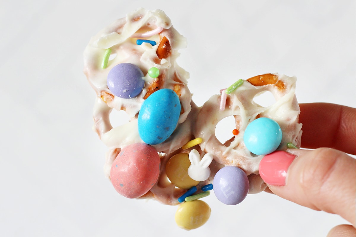 A woman's hand holding a piece of Easter White Chocolate Pretzel Bark with bunny sprinkles.
