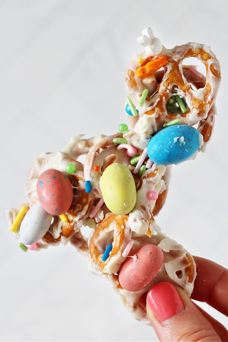 A woman's hand holding a piece of Easter White Chocolate Pretzel Bark with Robin Eggs.