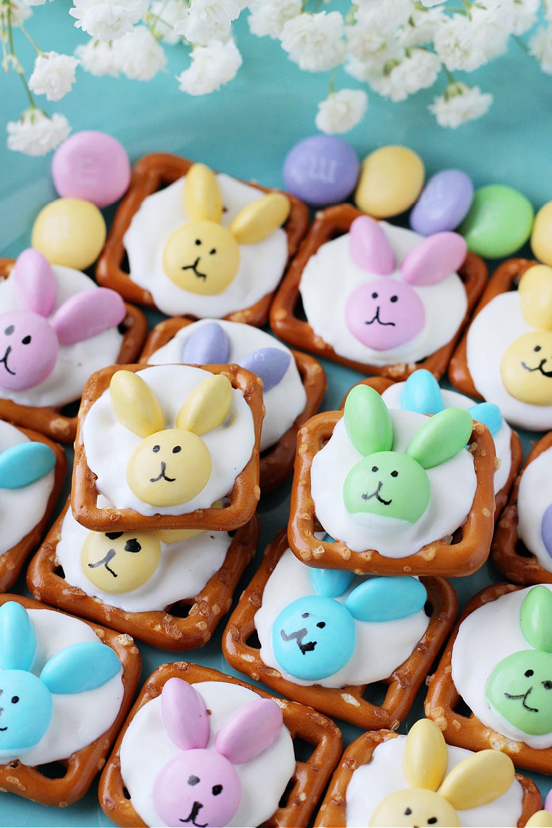 Easter bunny pretzels stacked on a blue plate with white flowers and pastel M&Ms.