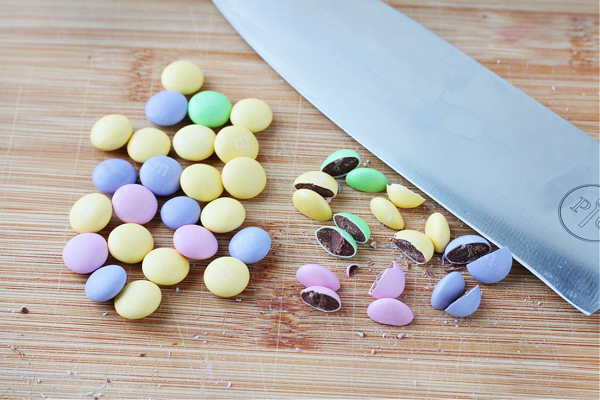 Pastel M&Ms on a wooden cutting board with a knife cut in half.