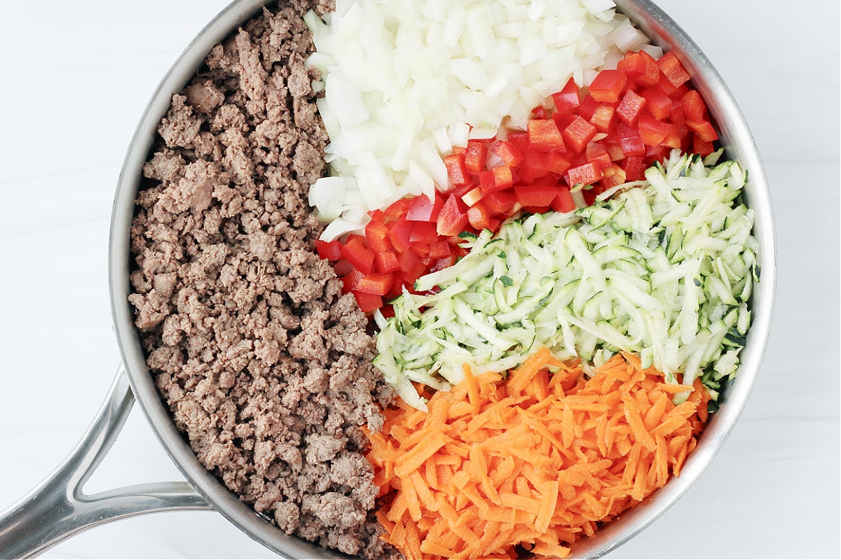 Overhead photo of browned ground meat, chopped onion and peppers and shredded zucchini and carrots.