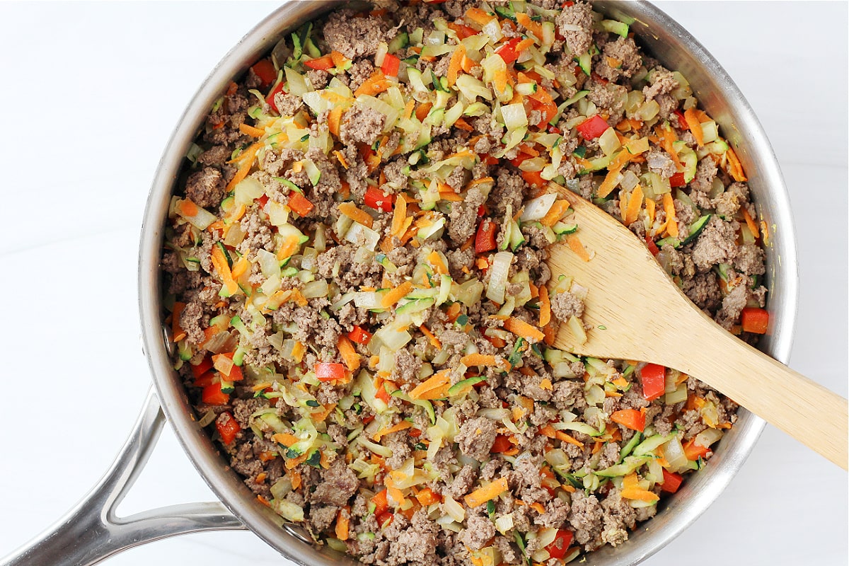 Overhead photo of browned ground meat and chopped vegetables being stirred in a skillet.