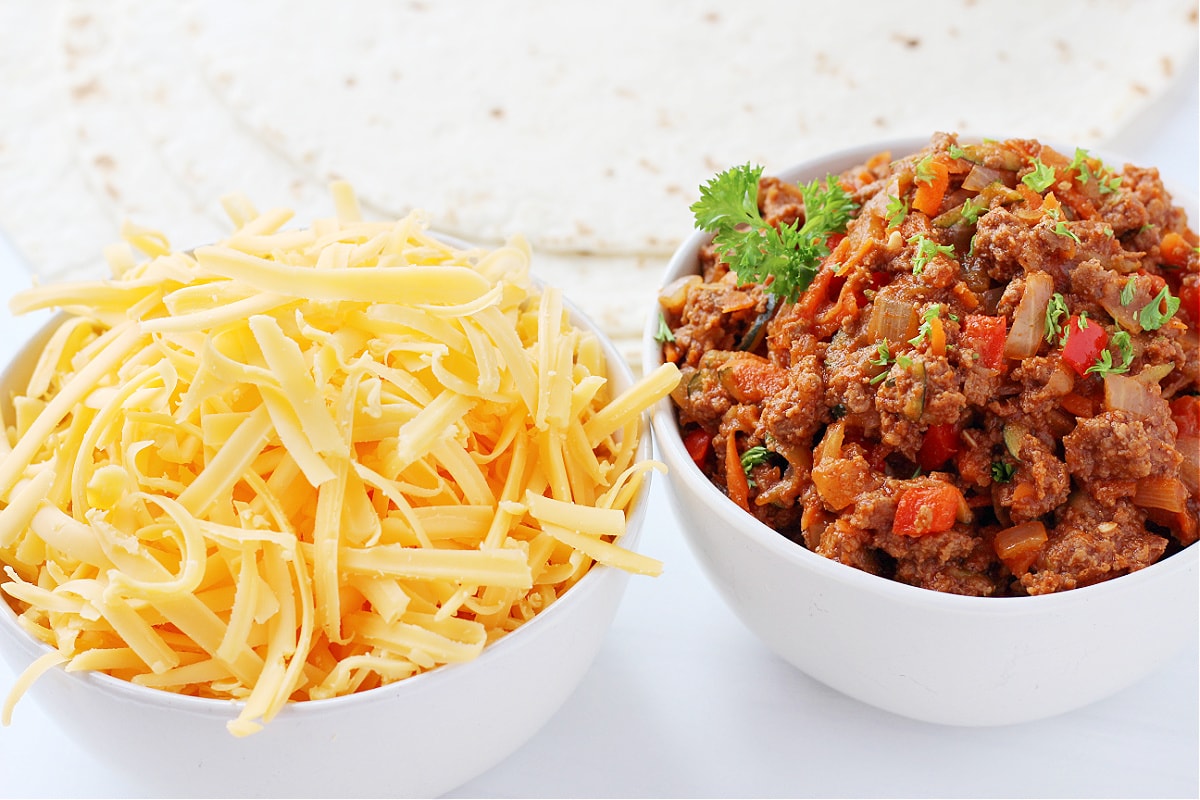 Up close photo of a bowl of sloppy joes, a bowl of cheese and tortillas.