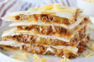 Four sloppy joe quesadilla wedges stacked on top of each other topped with shredded cheese.
