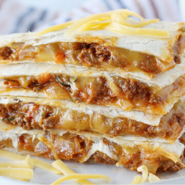 Four sloppy joe quesadilla wedges stacked on top of each other topped with shredded cheese.