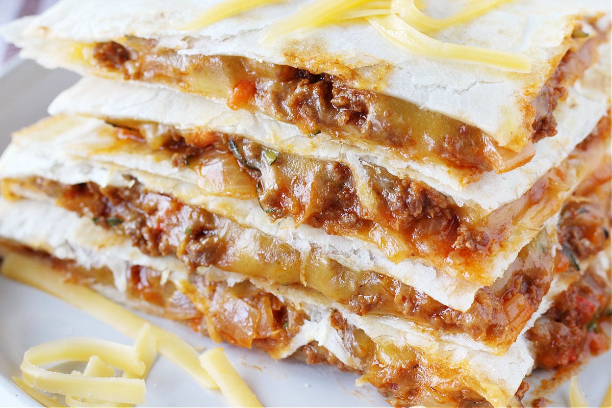 Up close photo of four sloppy joe quesadilla wedges stacked on a plate.