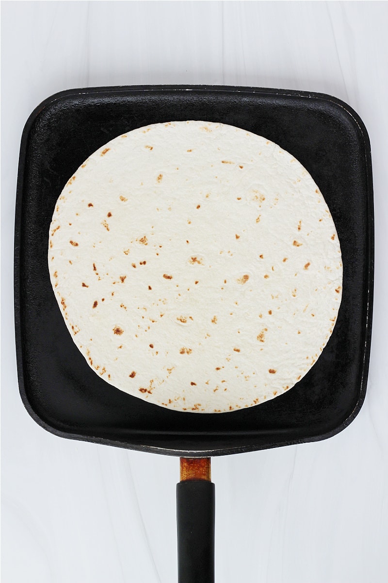 Overhead photo of a tortilla on a black stovetop pan.